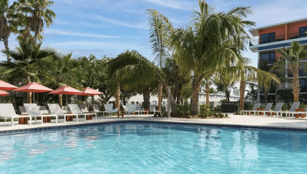 Hilton Garden Inn St Pete Beach Hotel, photo is of the pool area with palm trees and chairs in the background.