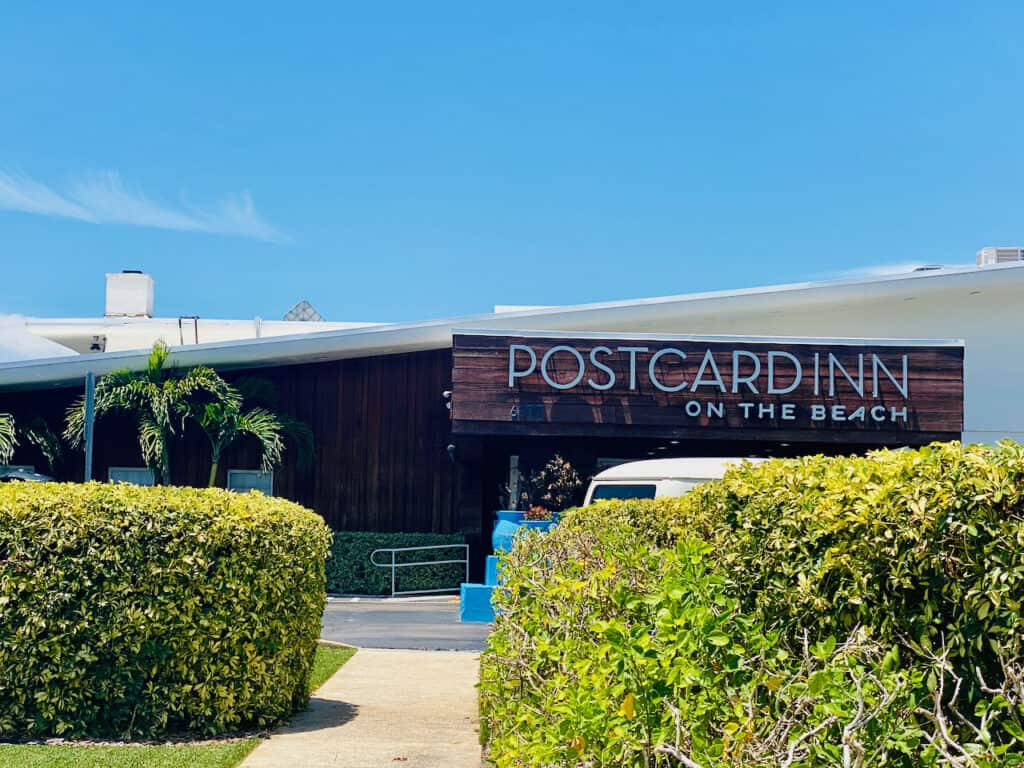 Post Card Inn St Pete Beach, PCI on the Beach sign and front entrance photo with green shrubs in front.