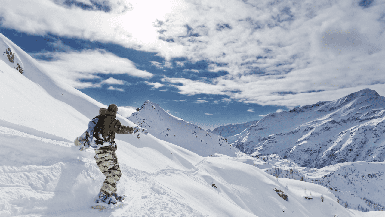 Snowboard trip in the Alps shows man snowboarding into the sun on the side of a mountain - while you can't snowboard in Paris. This is an ideal location reachable by train.