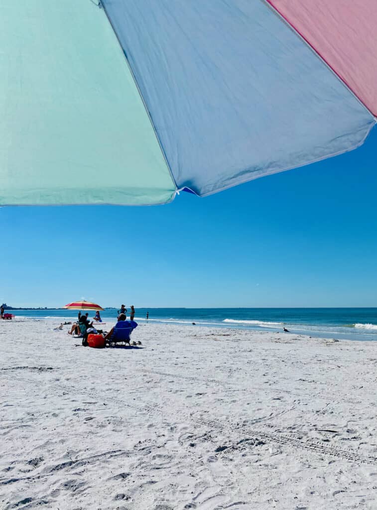 Sitting under a colorful umbrella on the white sand beach at Upham Beach Park.