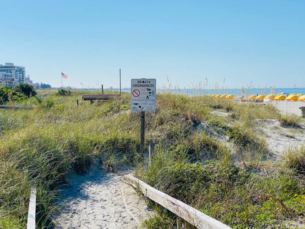 photo of the white sandy entrance to St Pete Beach with sea oats in the distance with yellow cabanas. 