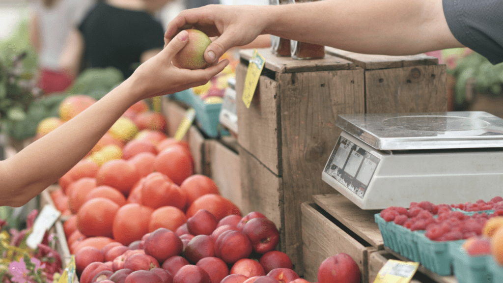 Farmers market with fresh fruit being purchased from a vendor.