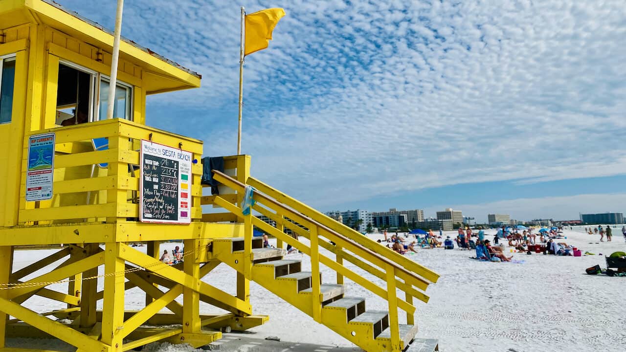 Siesta Key Beach Flag Warnings showing a yellow flag for caution: Are There Sharks in Siesta Key - the flags let you know when there is a concern. Beach goers in the distance.