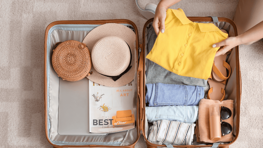 woman packing her suitcase with clothing items such as a hat, shirts, and sunglasses